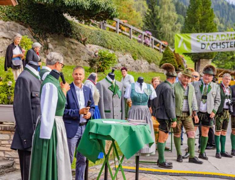 Mehrere Menschen in Tracht gekleidet am Schutzengelkirchtag in Kleinsölk, umringt von Schaufensterpuppen des Steirischen Heimatwerks mit original steirischen Trachten.